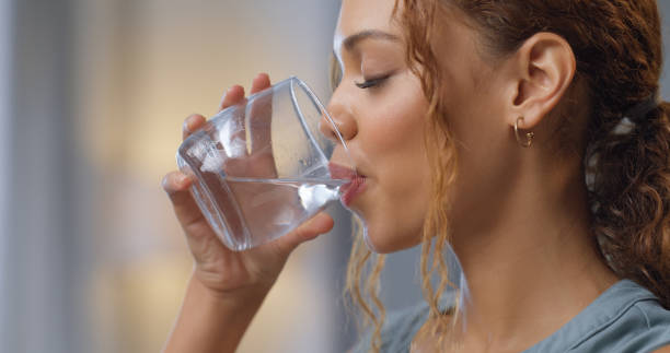 Vértes egy nőről, aki egy pohár vizet iszik a hidratálásért, a szomjúságért és az egészségért a házában.Boldog lány wellness-el, diétával és egészséges életmóddal, egy friss vízi italt élvezve, miközben otthon pihen.