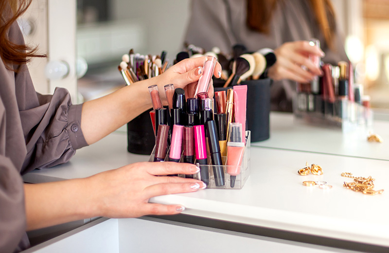 Young woman is neatly organizing her lipstick, lip gloss in the makeup storage and putting into dressing table drawer. Concept of storing personal makeup beauty product in organizer.