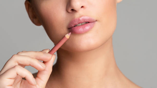 Концепт лепоте.Жена црта усне голим ружичастим оловком за усне преко сиве позадине, обрезивање